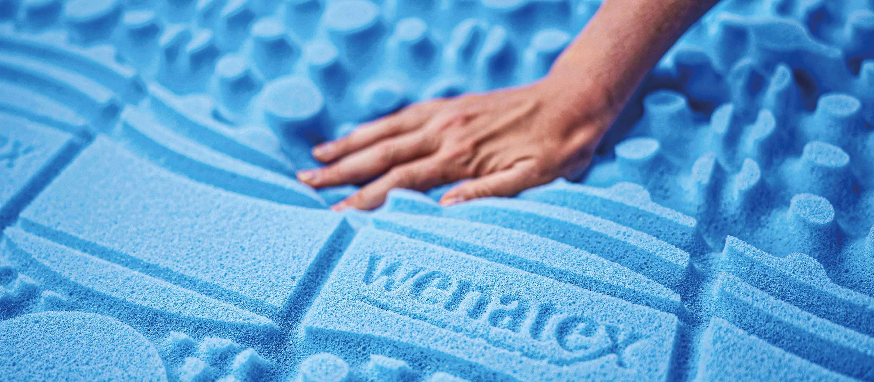 Hand berührt den blauen Matratzenkern mit dem Logo von Wenatex.