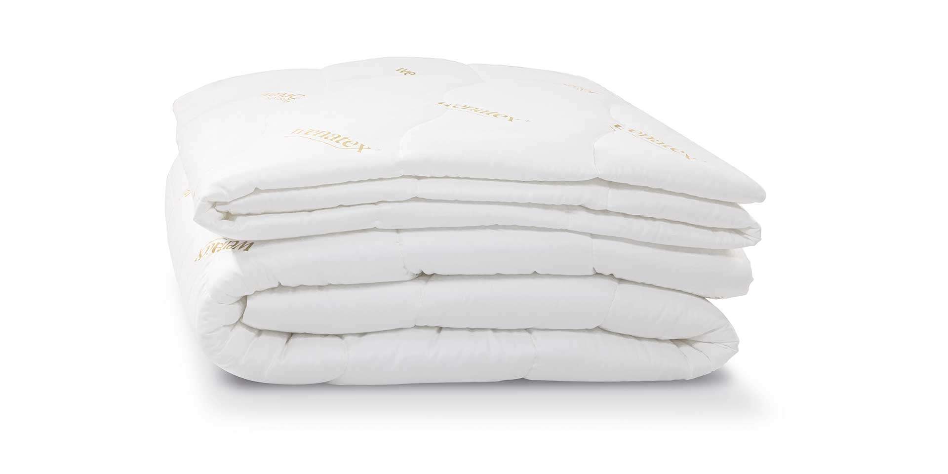 Gestapelte, weiße Bettdecken mit einem strukturierten Obermaterial auf hellem Hintergrund.