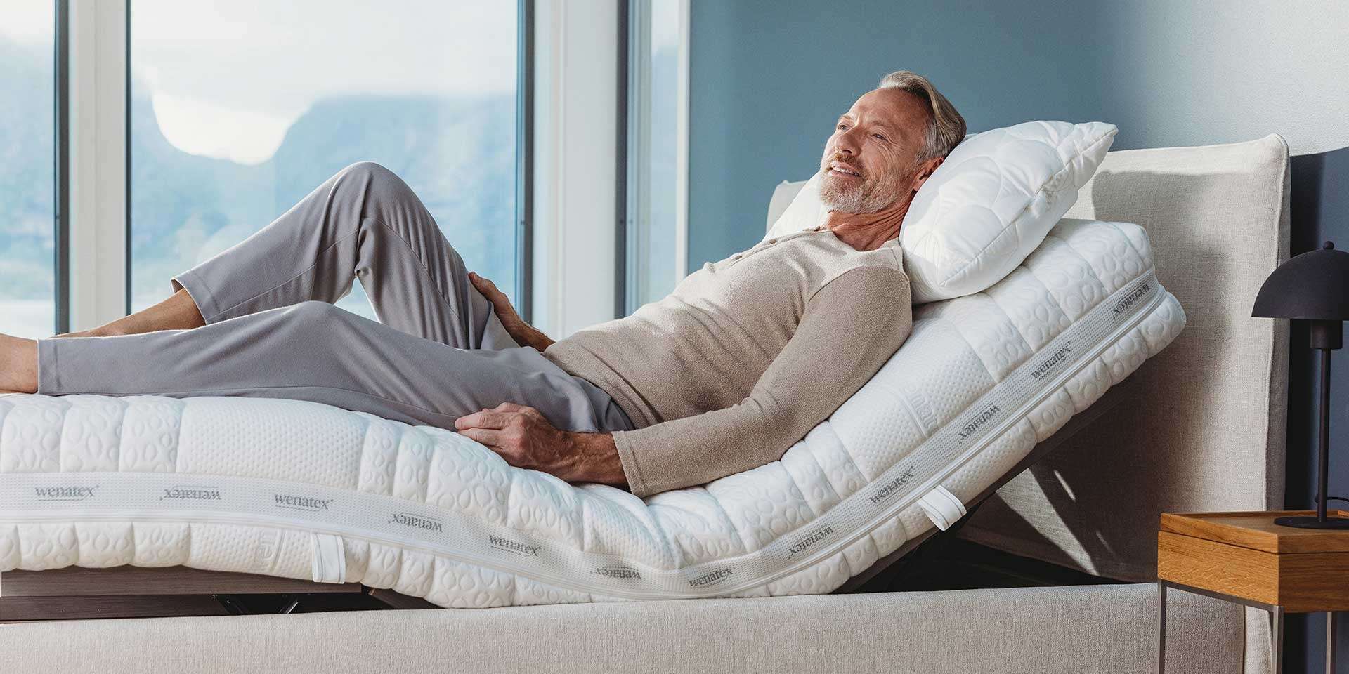 Ein älterer Mann entspannt auf einem verstellbaren Bett mit Kopf- und Fußteil in einem hellen Raum.