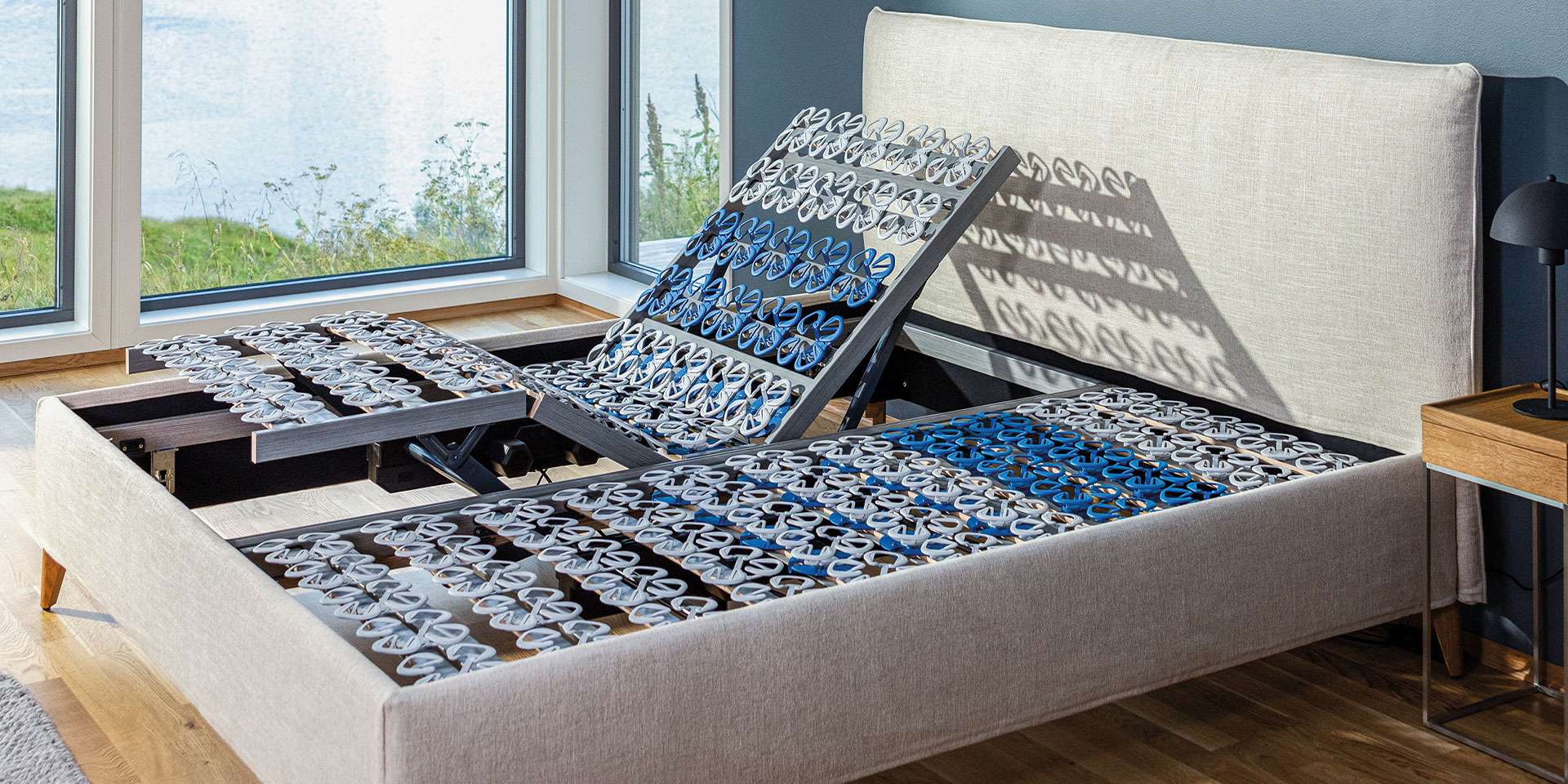Slatted frame in a modern bed frame with adjustable head and foot sections, in front of a window.