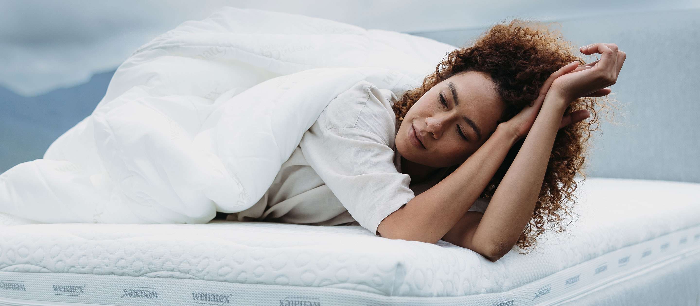 Woman lying relaxed on a mattress covered with a blanket outdoors.