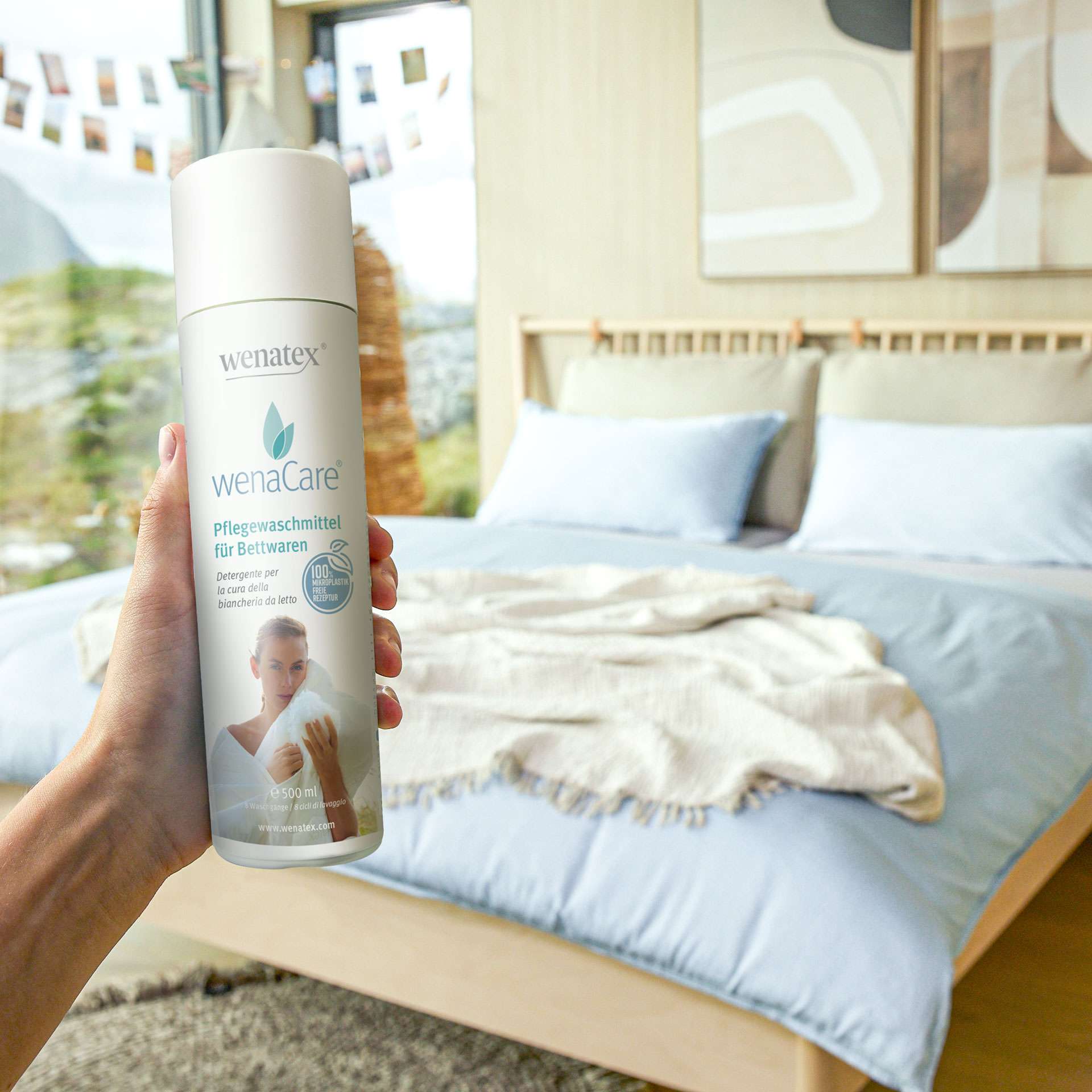 Hand holding Wenatex care detergent for bedding in front of a bedroom with a bed and blanket.
