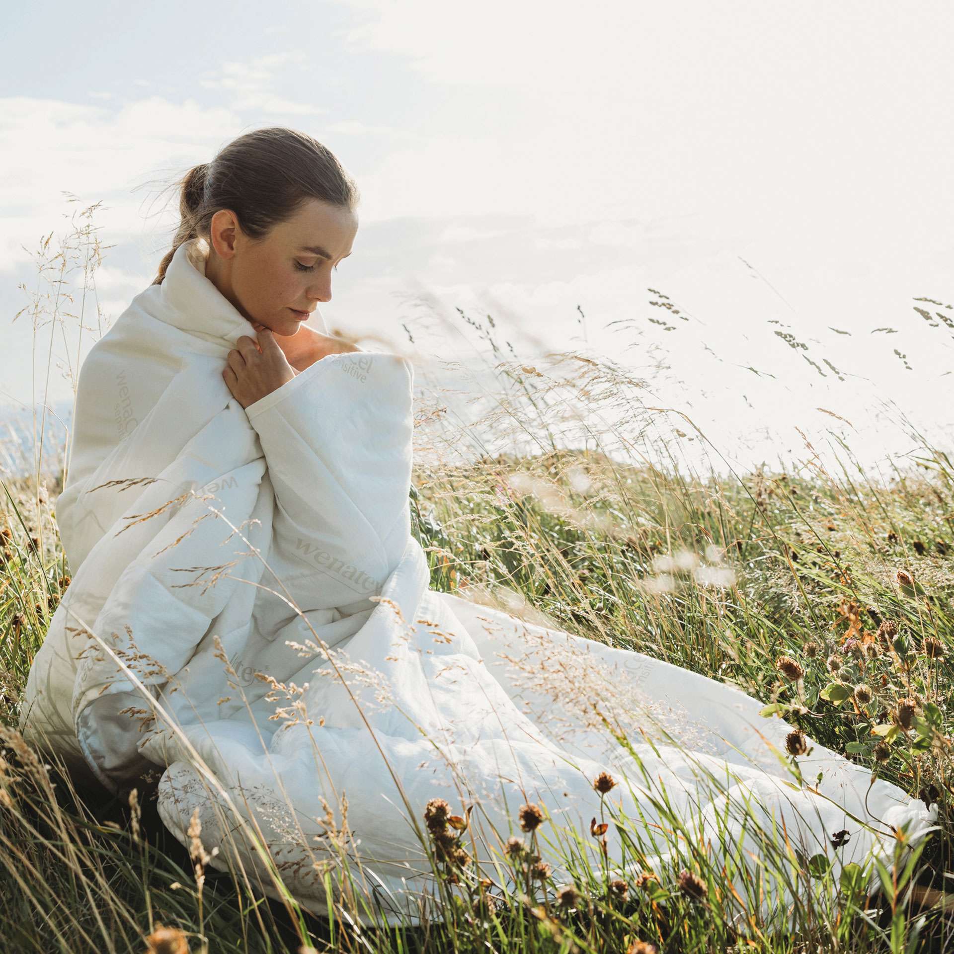 Woman in a meadow, wrapped in a light white blanket from Wenatex.