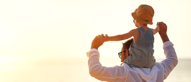 Vater trägt sein Kind auf den Schultern im Sonnenlicht