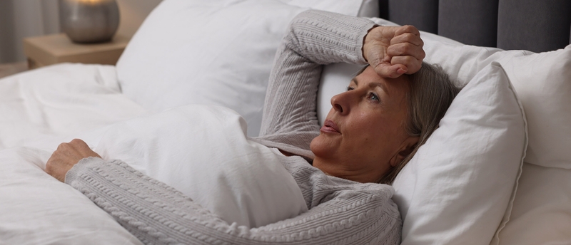 Eine Frau liegt im Bett und fasst sich mit der Faust an die Stirn