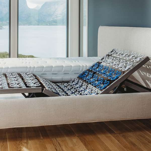 Bett mit Lattenrost und Matratze, Blick auf eine Landschaft durch ein großes Fenster.