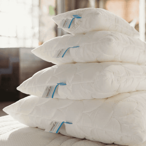 Vier stapelweise angeordnete, weiße Kissen mit blauen Etiketten auf einem Bett.